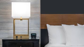 Una cama bien hecha con ropa de cama blanca, una mesita de noche con una lámpara y un reloj digital, y una pared con diseño de paneles de madera.