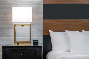 A neatly made bed with white linens, a bedside table with a lamp and a digital clock, and a wall with a wood panel design. - DoubleTree by Hilton Denver - Aurora (Aurora)