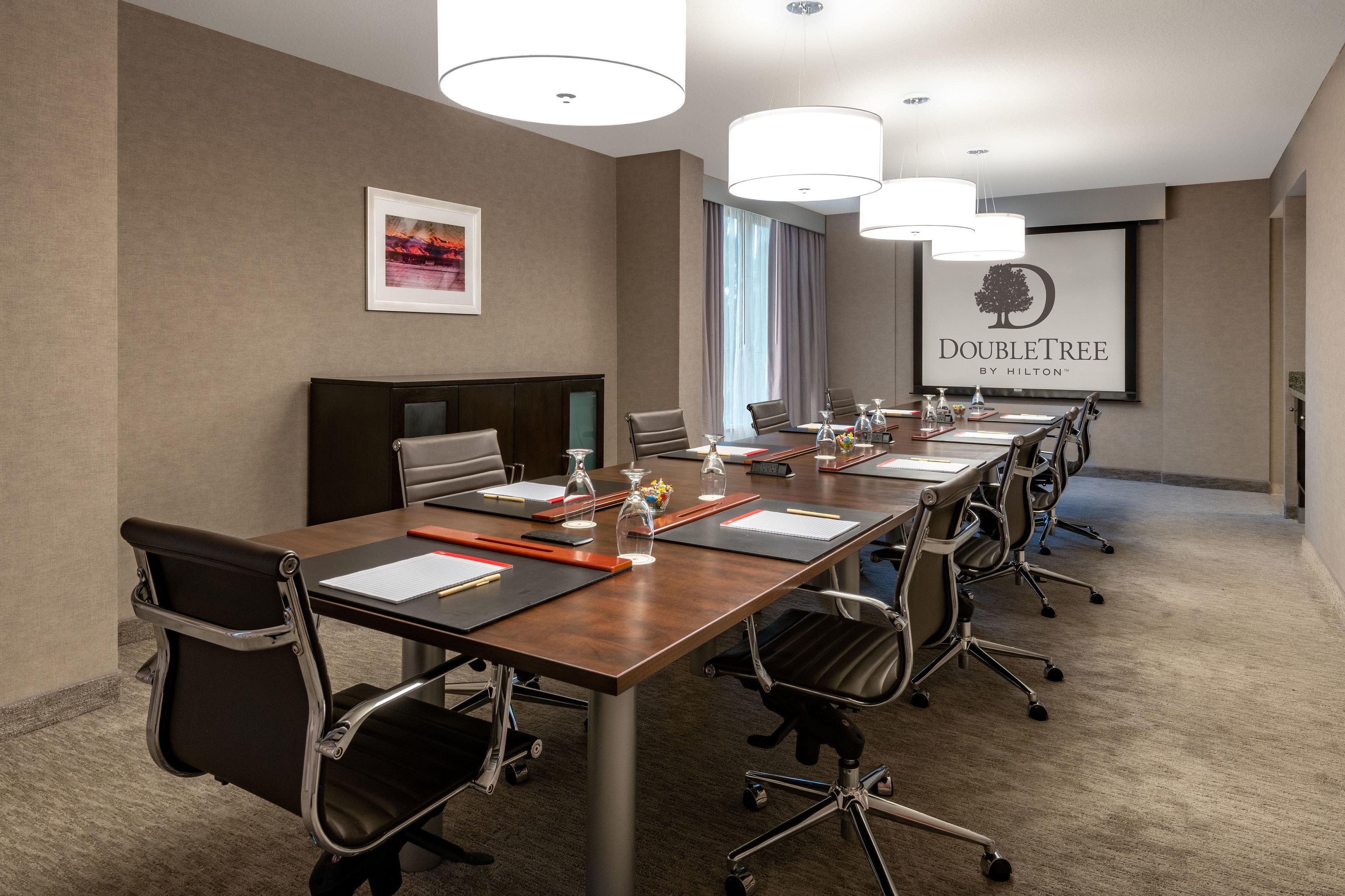 A conference room with a long table, multiple chairs, and a presentation screen.