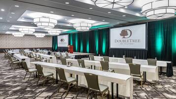 A conference room with long tables and chairs, a podium, and a large screen displaying the DoubleTree logo.