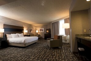 A hotel room with a large bed, a desk, a chair, a desk lamp, a TV, a bathroom with a sink and mirror, and a carpeted floor. - DoubleTree by Hilton Denver - Aurora (Aurora)