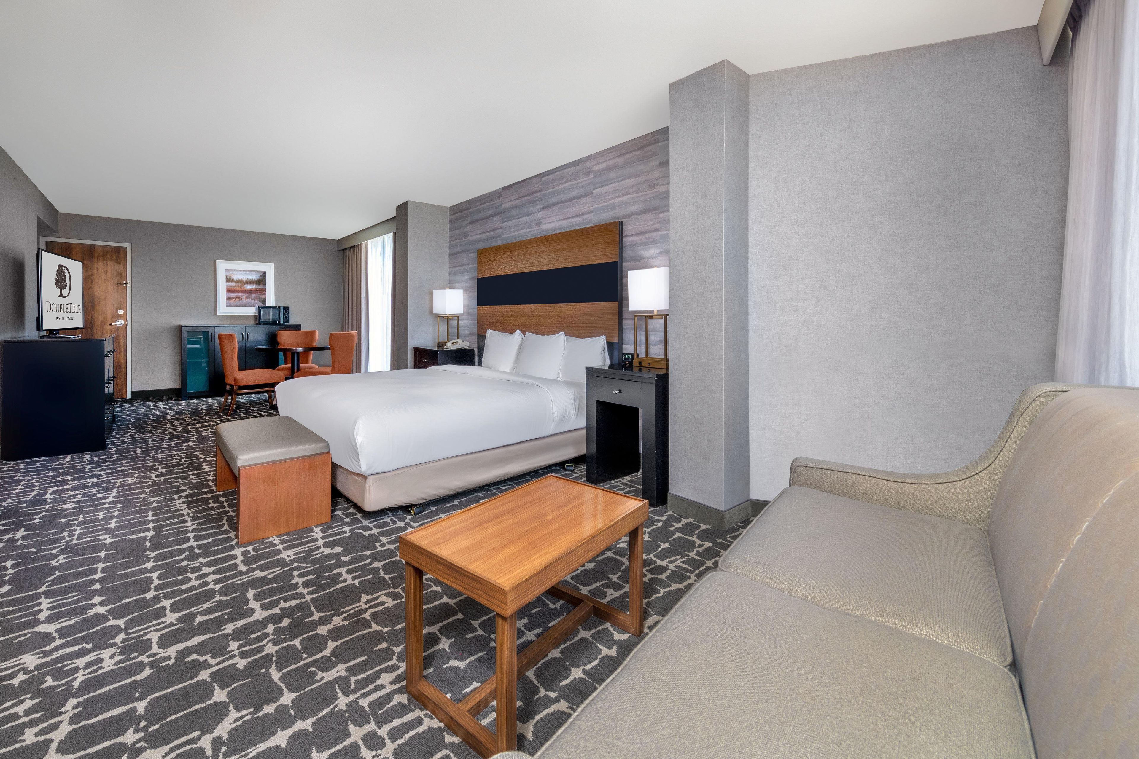 Una habitación de hotel con una cama, una mesa de centro de madera, un sofá, un escritorio con una silla y un televisor.