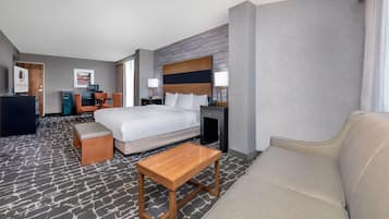 Una habitación de hotel con una cama, una mesa de centro de madera, un sofá, un escritorio con una silla y un televisor.