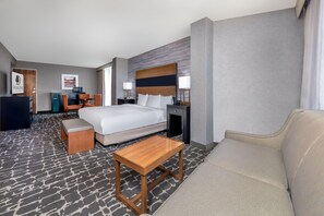 Una habitación de hotel con una cama, una mesa de centro de madera, un sofá, un escritorio con una silla y un televisor.