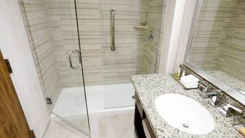 A modern bathroom with a glass-enclosed shower, a granite countertop, and a large mirror.