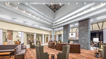 A spacious lobby with multiple seating areas, a central column, and a ceiling with linear lighting.
