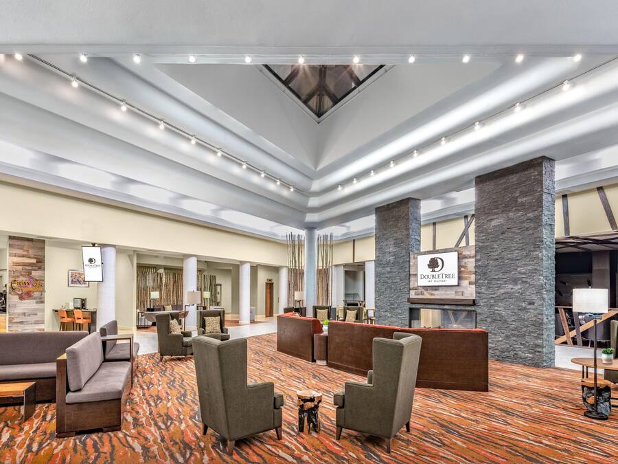 A spacious lobby with multiple seating areas, a central column, and a ceiling with linear lighting.