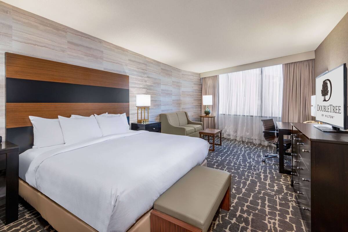 A hotel room with a large bed, a desk, a chair, and a TV.