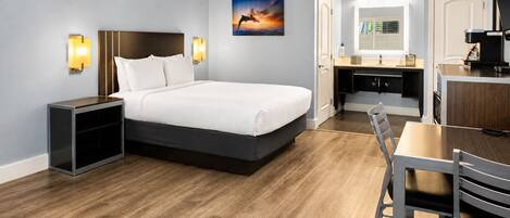 A hotel room with a bed, bedside table, desk, and chair.