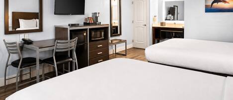 Habitación de hotel con cama, escritorio con silla, televisión, microondas, cafetera y espejo de baño.