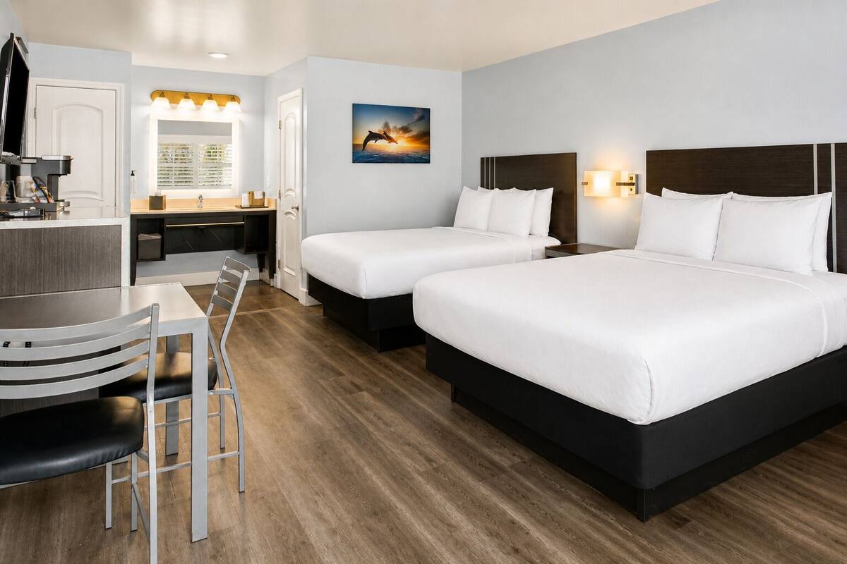 A hotel room with two beds, a desk, a chair, a mirror, and a painting on the wall.