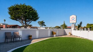 Un área exterior vallada con césped artificial, un letrero de Pacific Inn Monterey y una fila de sillas.