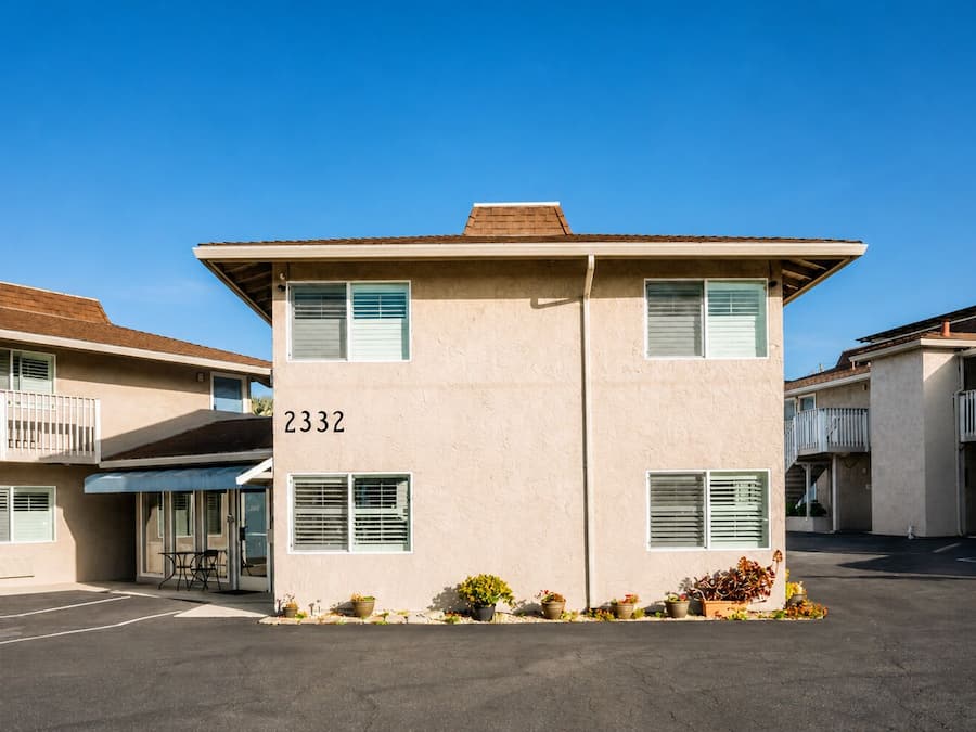 A two-story motel with a beige exterior, numbered 2332, featuring a covered entrance and a parking lot.