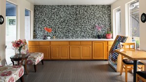 Una cocina con armarios de madera, salpicadero de azulejos, una mesa de comedor con sillas y una mesita auxiliar con un florero.