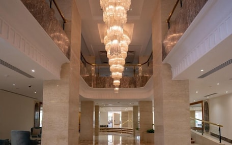 A spacious lobby with a large chandelier, marble flooring, and a central circular design.