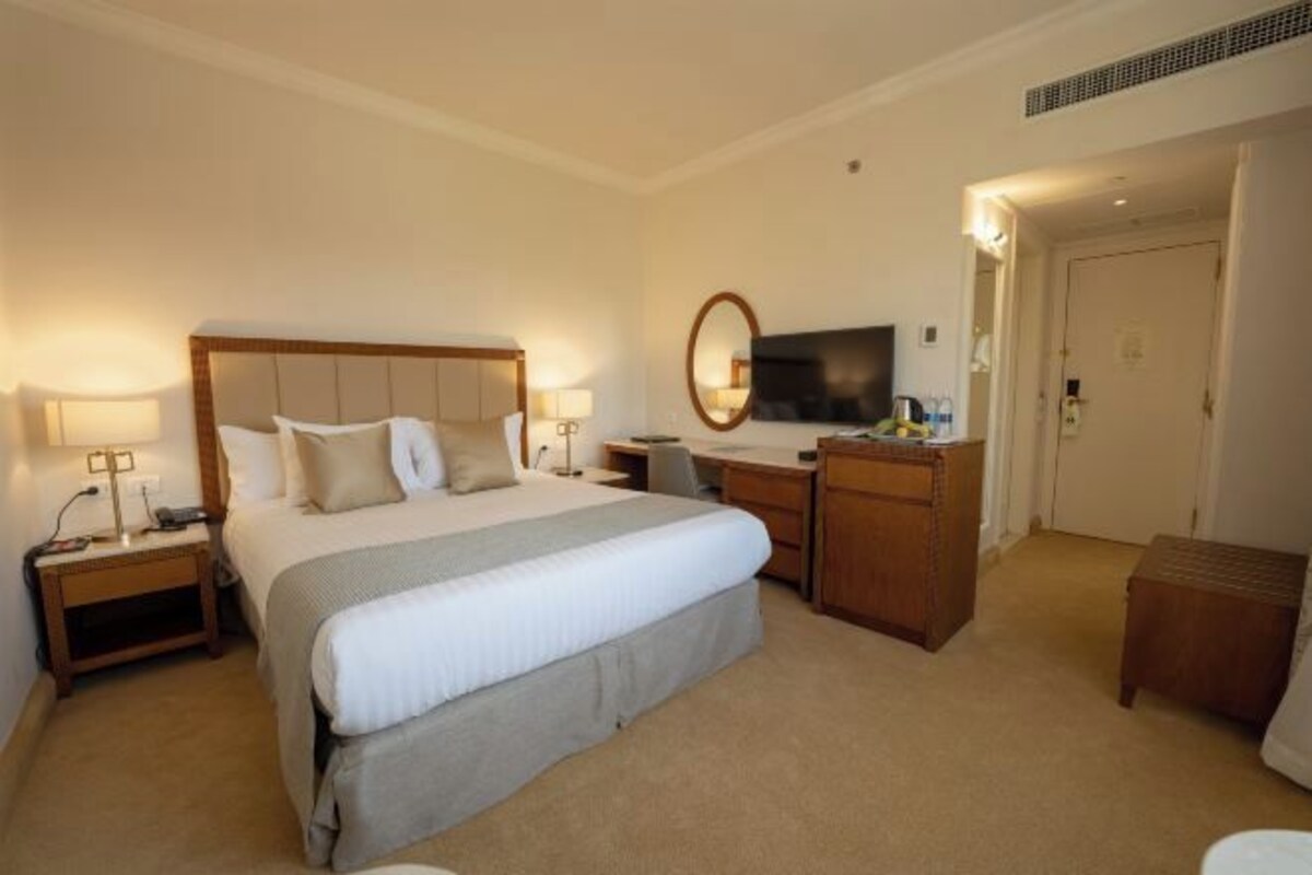 A hotel room with a large bed, bedside tables, a desk, a chair, a television, and a mirror.