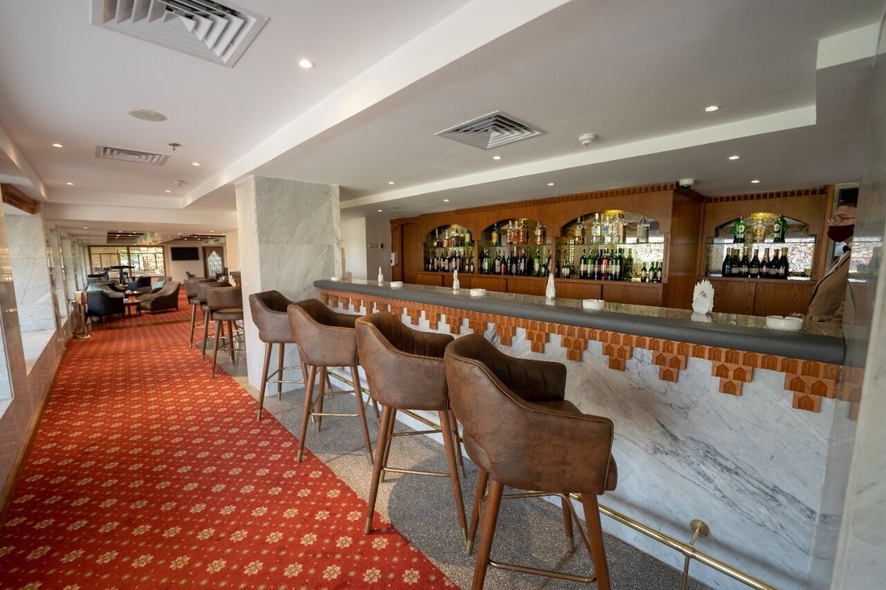 A bar area with a marble counter, multiple stools, and a red carpeted walkway.
