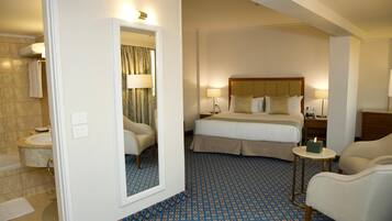 A hotel room with a large bed, a sitting area with a chair, a small table, and a mirror.