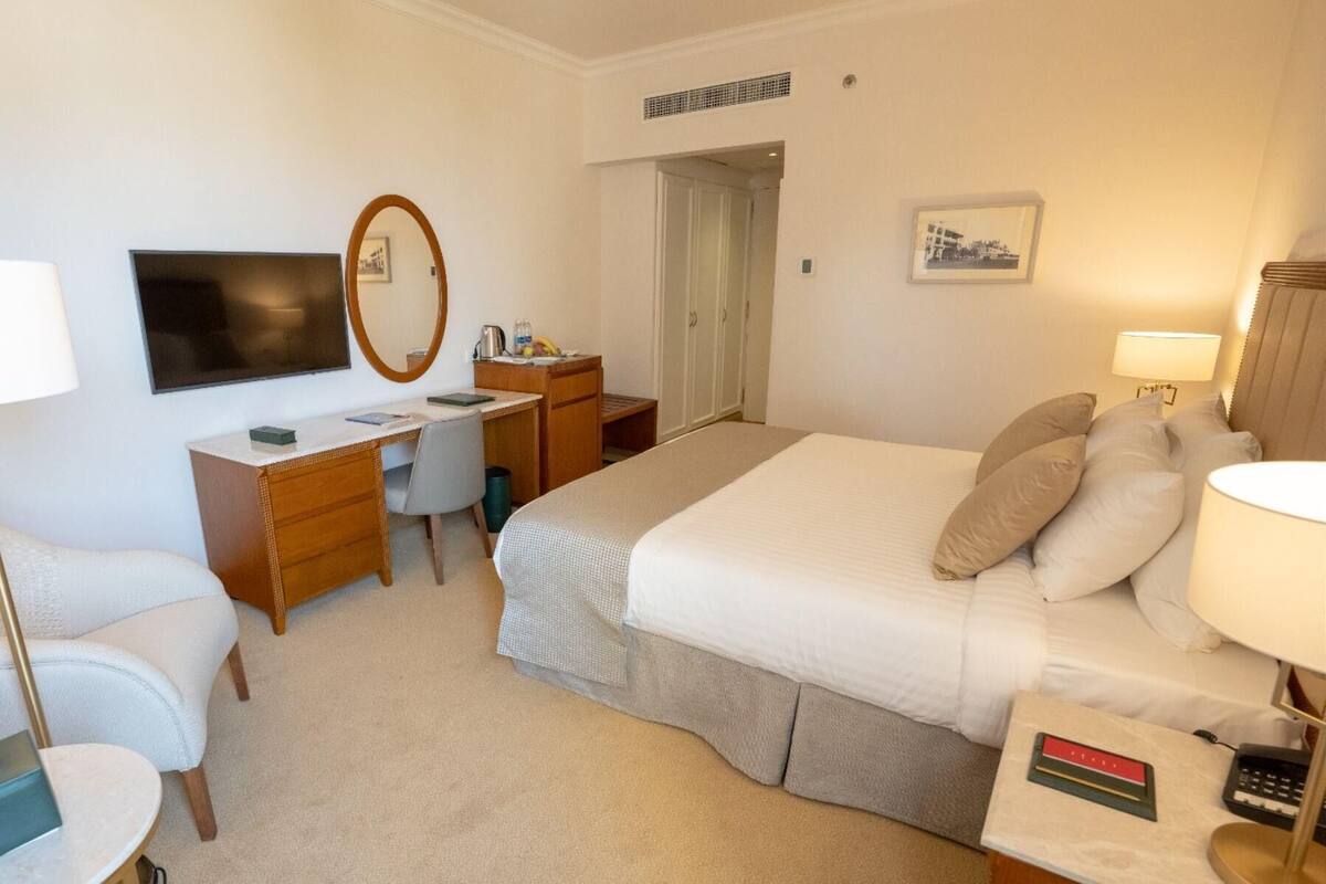Habitación de hotel con cama, escritorio, silla, televisor y una mesita con lámpara.