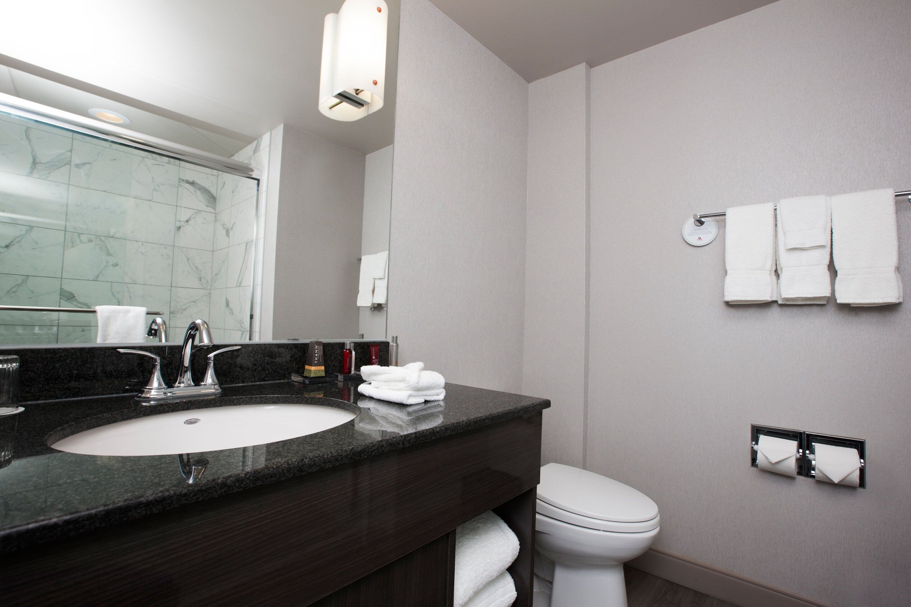 Une salle de bain moderne avec un lavabo en granit foncé, des toilettes blanches et un porte-serviettes sur lequel sont pliées des serviettes.