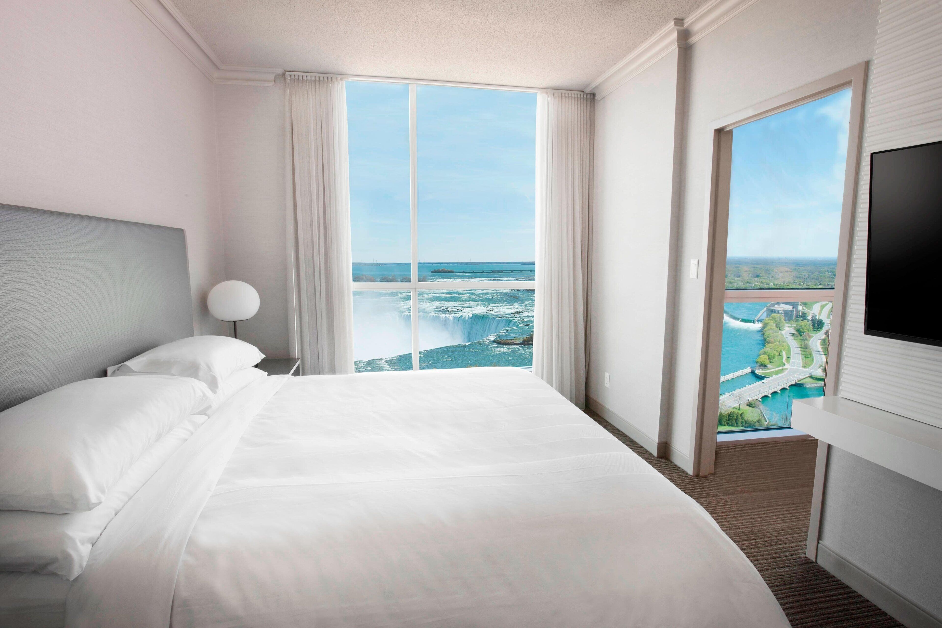 A hotel room with a large bed, a TV, and a view of a coastal landscape.