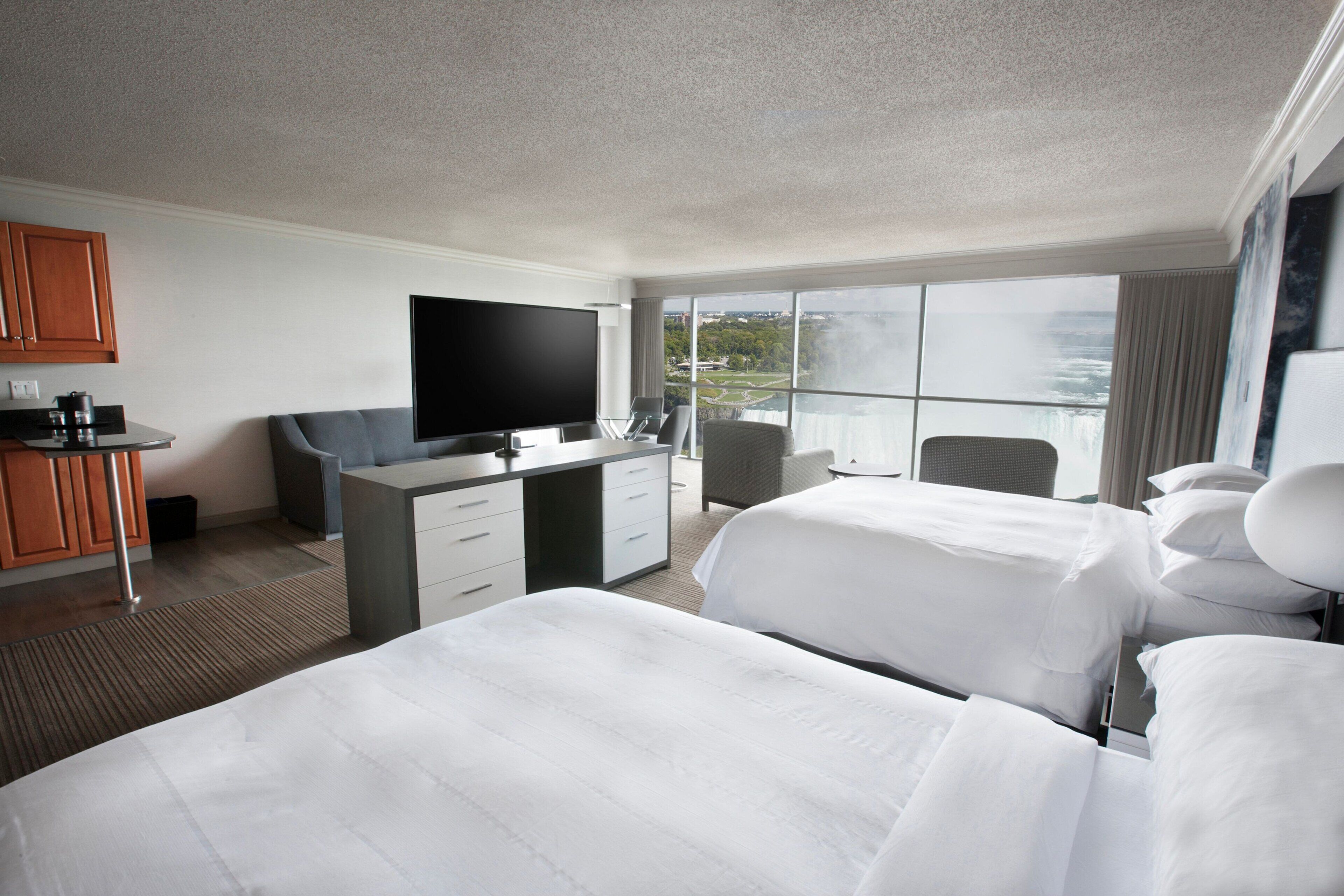 Habitación de hotel con dos camas, un escritorio, un televisor de pantalla plana, una silla y vistas a una cascada.