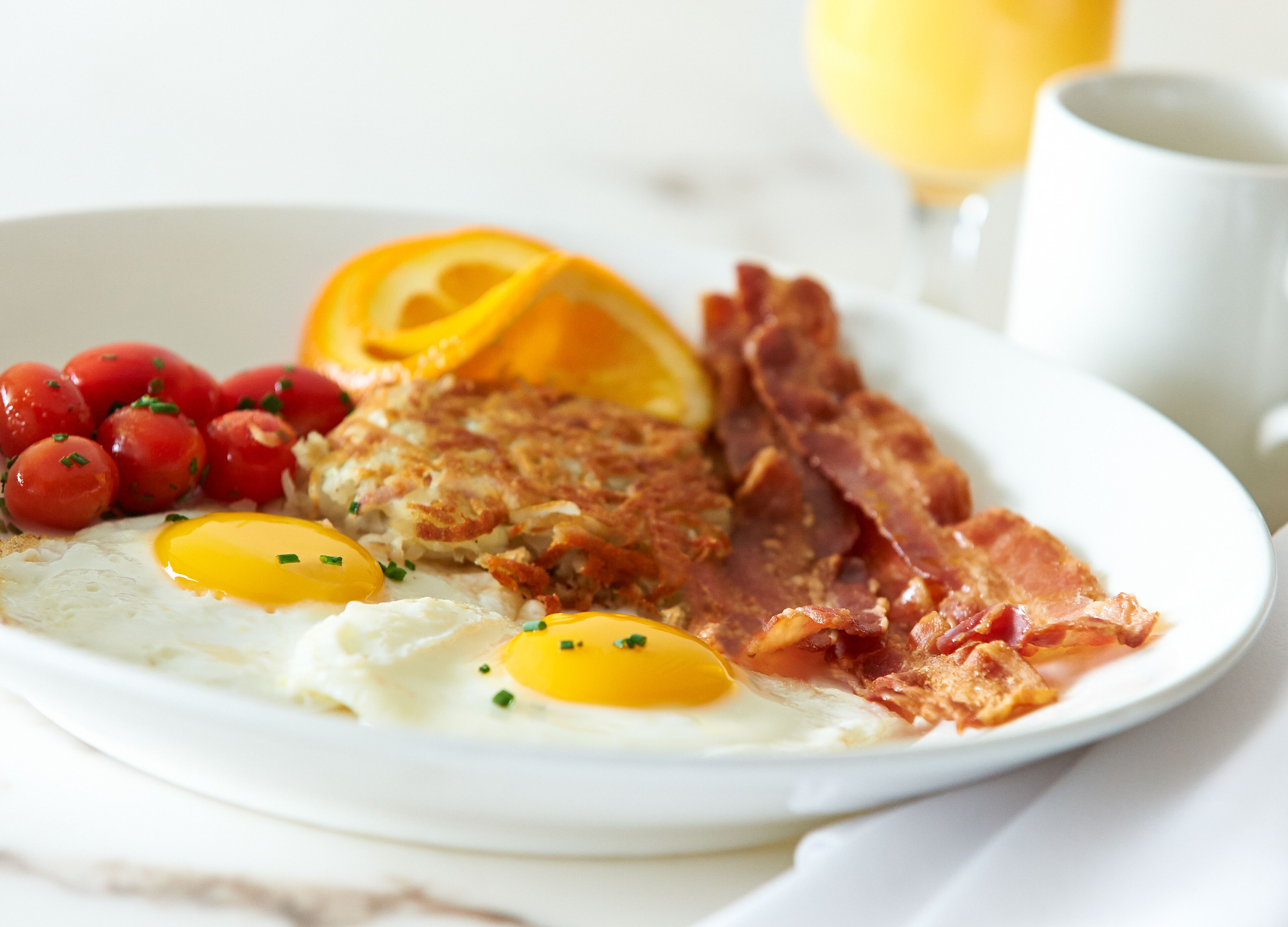 A plate with eggs, bacon, tomatoes, and a slice of orange.