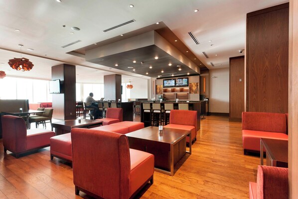 A modern restaurant with red seating, wooden flooring, and a bar area with a TV screen.