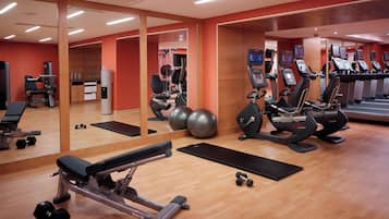 Un gimnasio con equipo de ejercicio, espejos y suelo de madera.