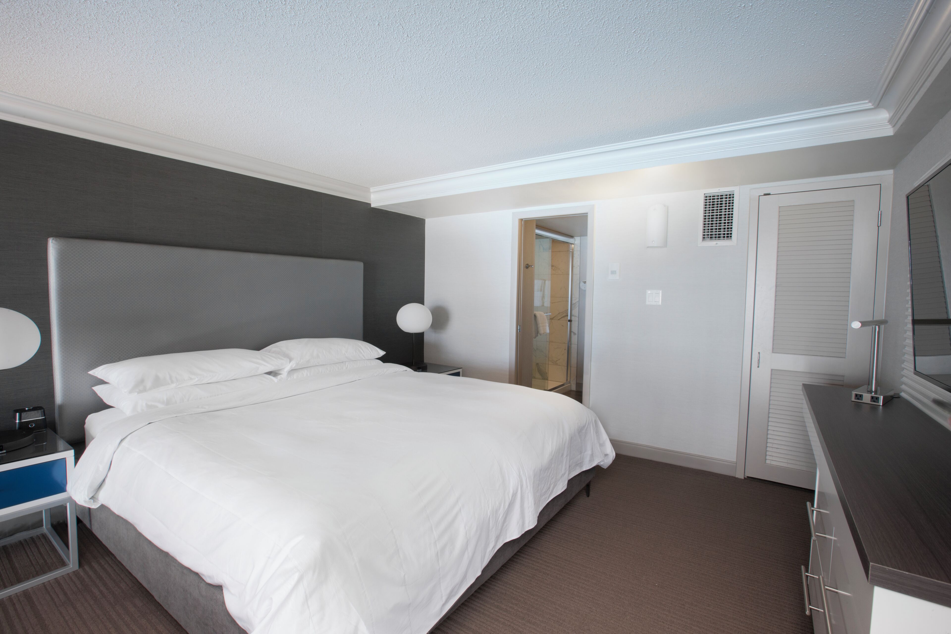 A modern hotel room with a large bed, bedside tables, a desk, and a wardrobe.