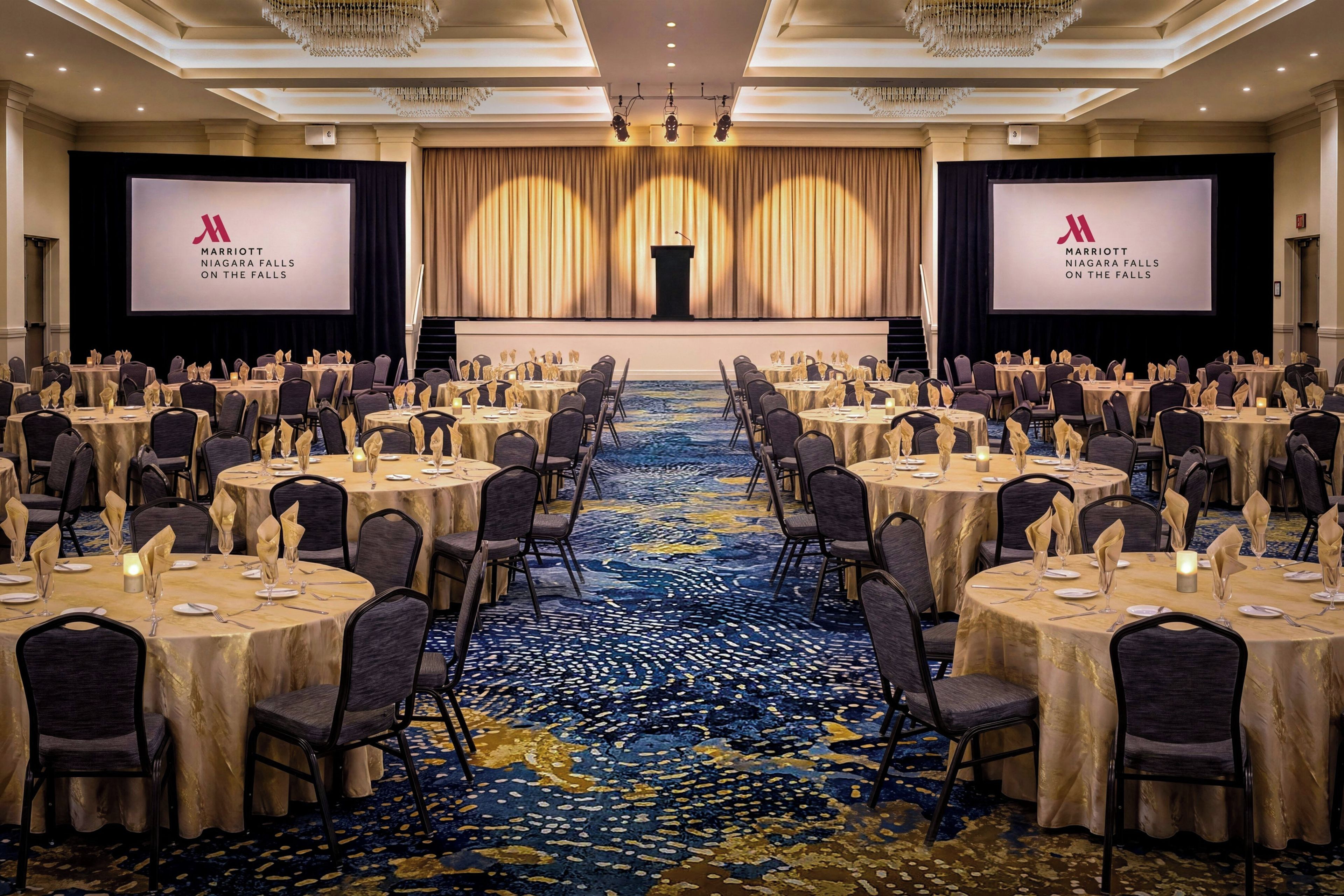 A conference room with multiple round tables, chairs, and a stage with a podium.