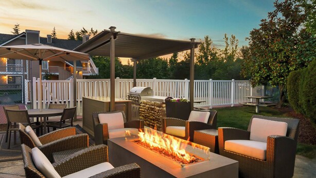Un patio al aire libre con una chimenea, mobiliario de mimbre, una parrilla y una zona de estar cubierta.