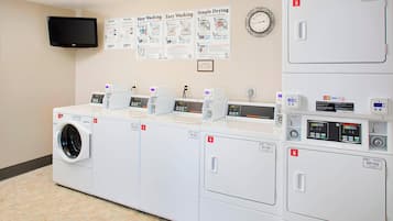 A laundry facility with multiple washing machines and dryers, numbered from 1 to 6, and a wall-mounted clock.