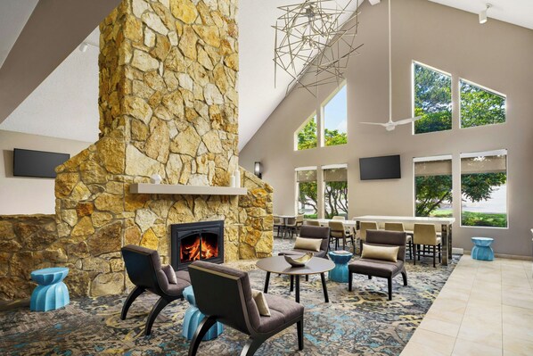 Un espacio interior amplio con chimenea de piedra, asientos cómodos y grandes ventanales con vistas al exterior.