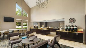 Un amplio salón con asientos cómodos, una estación central de café y un gran ventanal que proporciona luz natural.
