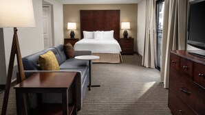 Una habitación de hotel con cama, sofá, una mesita, televisor y cómoda.