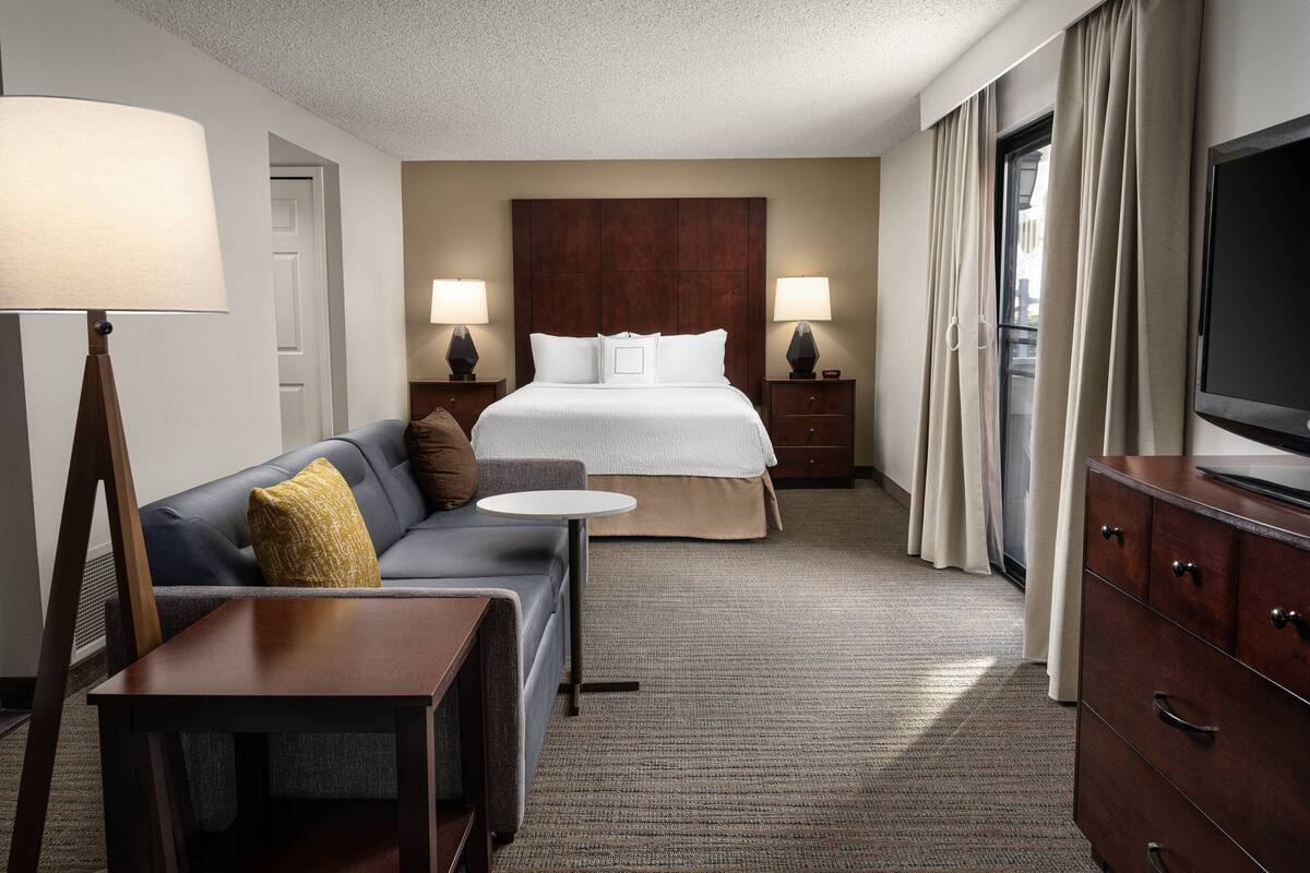 A hotel room with a bed, a sofa, a small table, a TV, and a dresser.