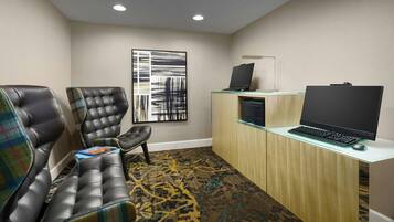 A conference room with leather chairs, a glass desk with a laptop, and a large abstract painting on the wall.