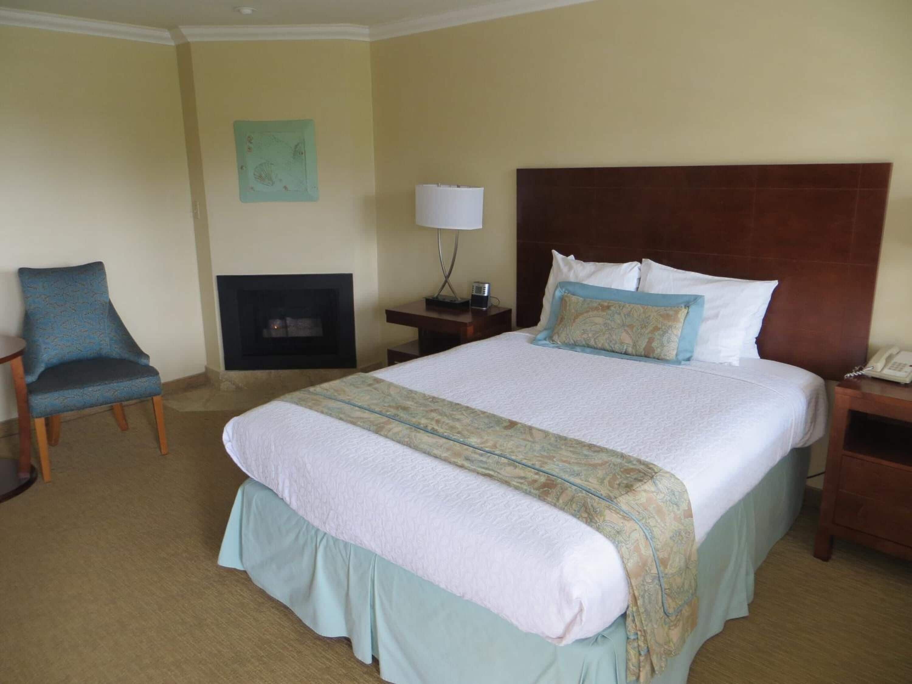 A hotel room with a large bed, a chair, a nightstand, a lamp, and a fireplace.