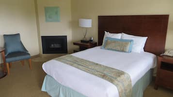 A hotel room with a large bed, a chair, a nightstand, a lamp, and a fireplace.