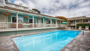 A swimming pool with a stone deck, a covered deck area with white railings, and hanging flower baskets. - Carmel Bay View Inn (Carmel)
