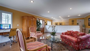 A spacious living room with a large sofa, a striped armchair, a glass coffee table, and a wooden cabinet. - Carmel Bay View Inn (Carmel)