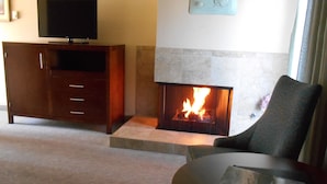 A living room with a fireplace, a television on a cabinet, and a chair with a book. - Carmel Bay View Inn (Carmel)