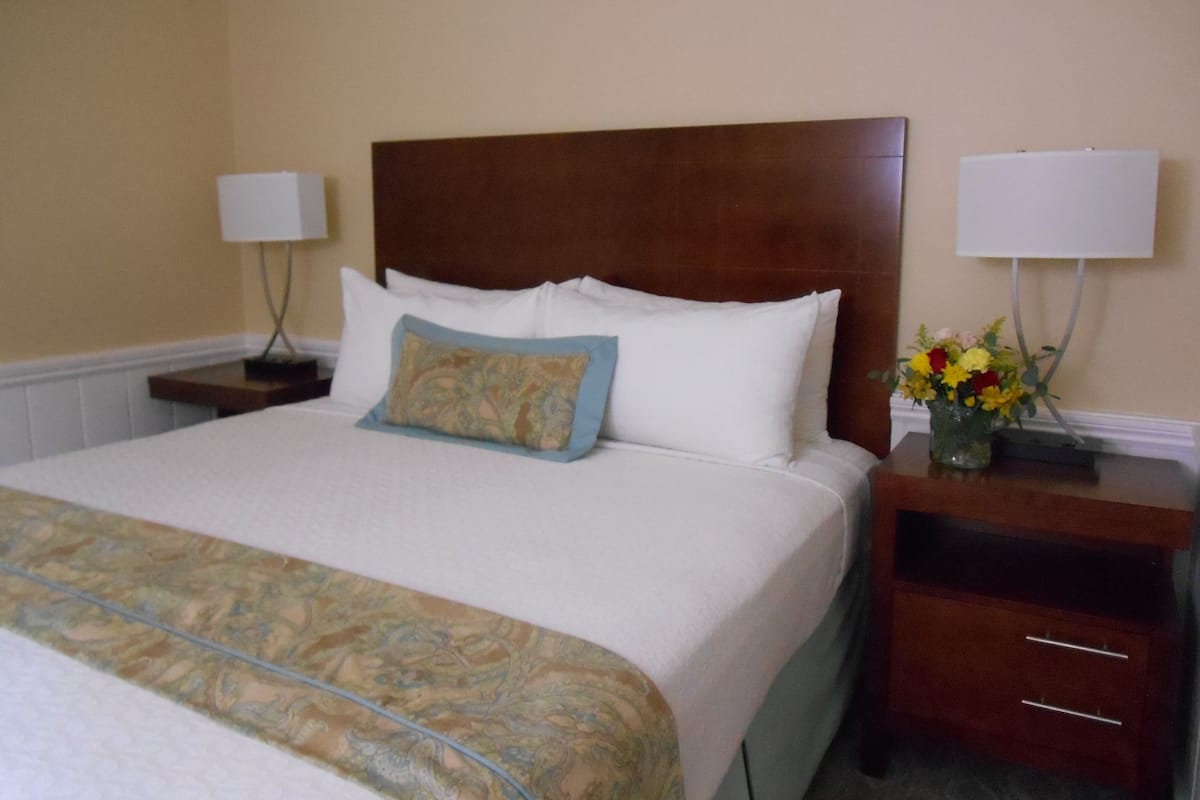 Una habitación de hotel con una cama grande, una mesita de noche con una lámpara y un jarrón con flores.