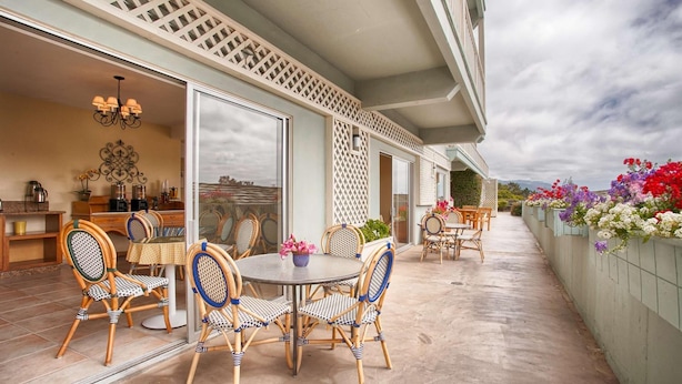 An outdoor patio with wicker furniture, a round table, and a view of the landscape. - Carmel Bay View Inn (Carmel)