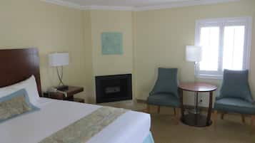 Habitación de hotel con una cama grande, una chimenea, dos sillones, una mesita y una ventana con persianas.