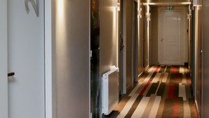 Un pasillo moderno de hotel con alfombra a rayas, un radiador y una puerta marcada con el número 215.