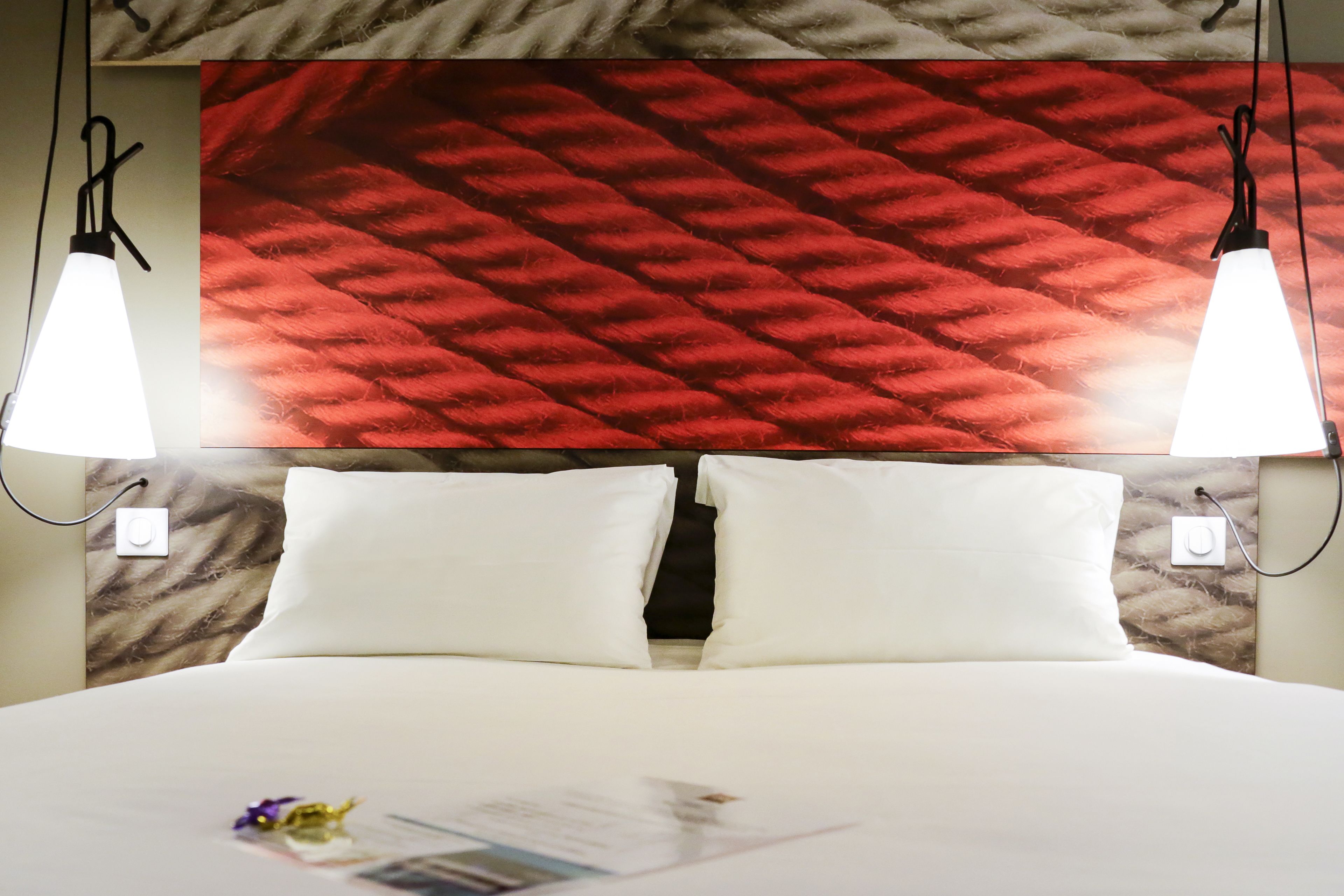 Ein Hotelzimmer mit einem großen Bett, zwei weißen Kissen und einer roten, strukturierten Wand dahinter.