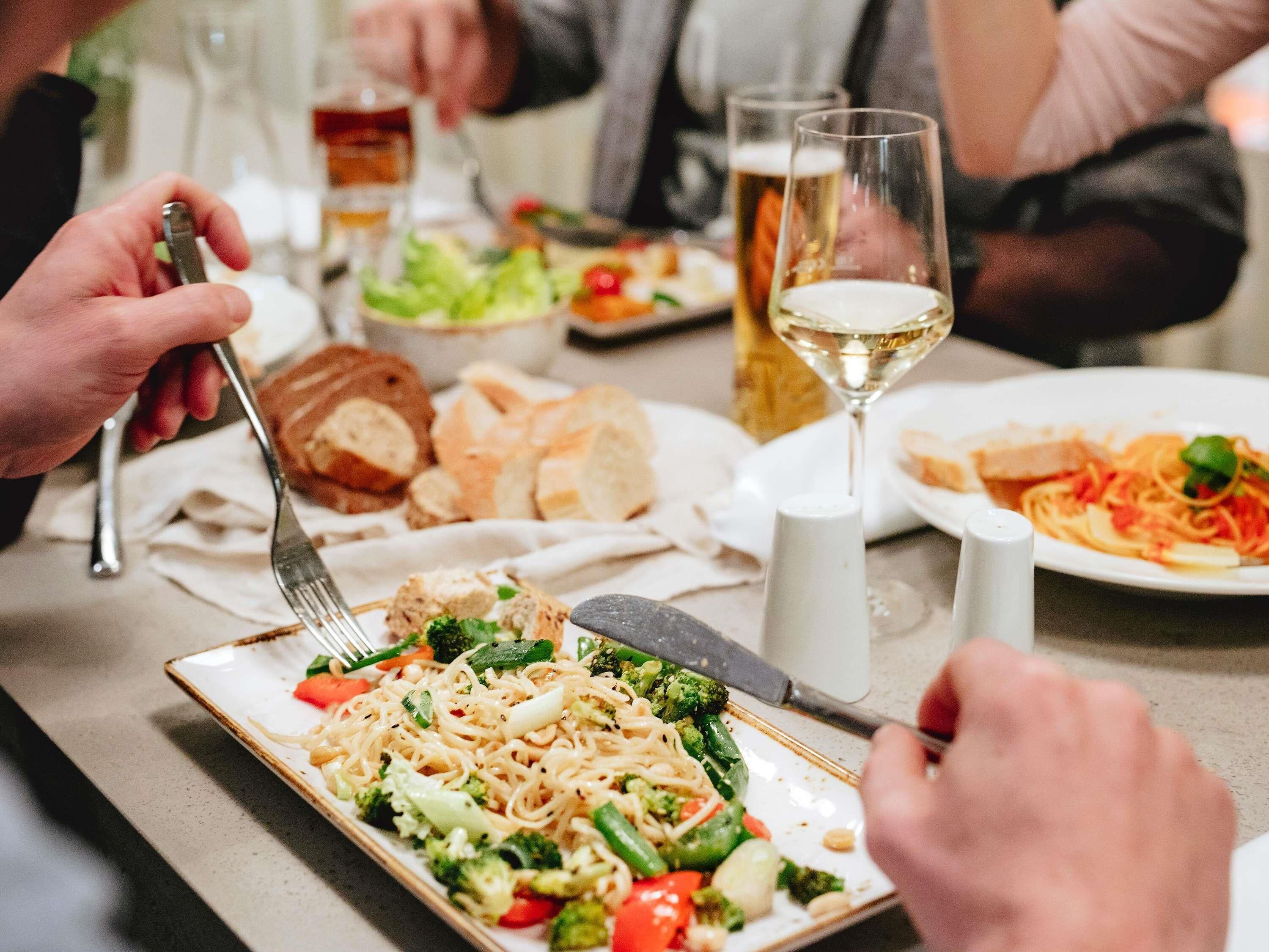 A dining table with various dishes, including pasta with vegetables, bread, and a glass of white wine.