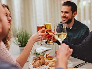 Un grupo de personas brindando con copas de cerveza y vino en una mesa con pan y un pequeño bol de fruta.